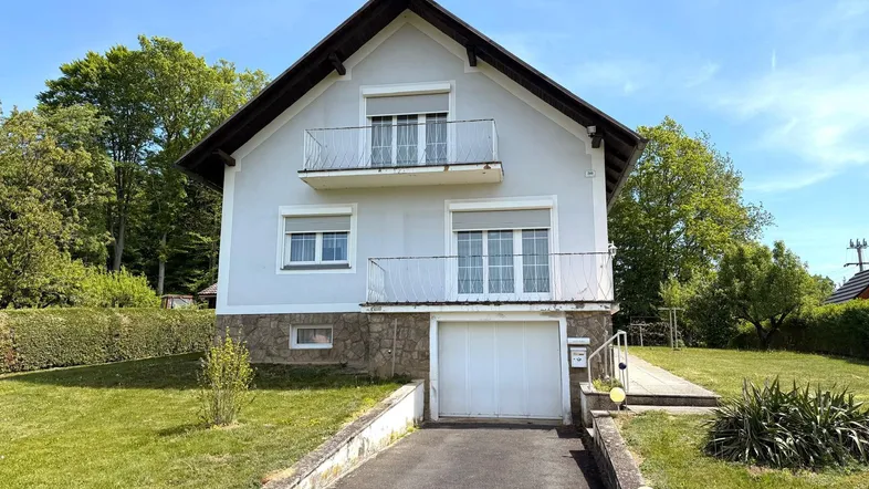 Vorderansicht des Hauses mit zwei Balkonen, Garage und gepflegtem Vorgarten.