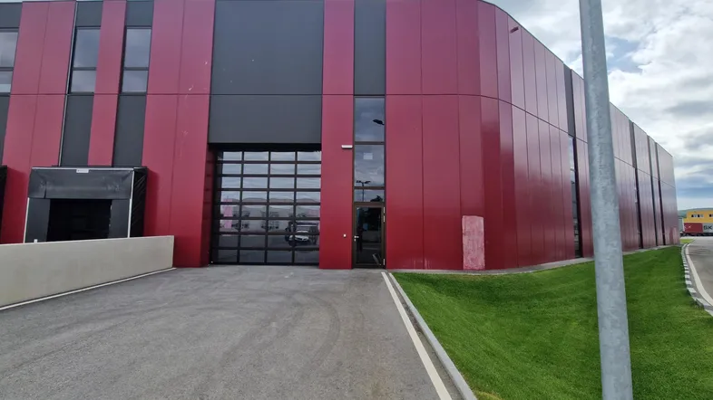 Modernes Industriegebäude mit roter und schwarzer Fassadenverkleidung sowie großen Rolltoren und Zufahrt.