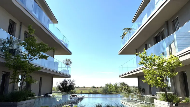 Moderne Wohngebäude mit Glasbalkonen und Blick auf einen ruhigen See unter blauem Himmel.