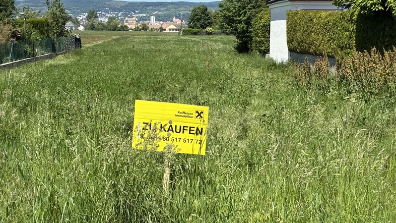 Großes Grundstück mit Verkaufsanzeige, umgeben von Grünflächen und Fernblick auf die Stadt.