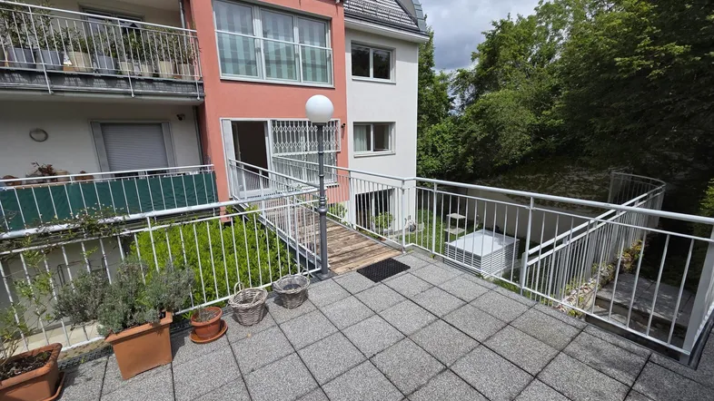 Geräumige Terrasse mit Fliesenboden, weißen Geländern und Blick auf den Gartenbereich.
