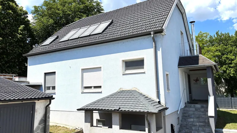 Modernes Einfamilienhaus mit heller Fassade, Satteldach und Solaranlage auf dem Dach.