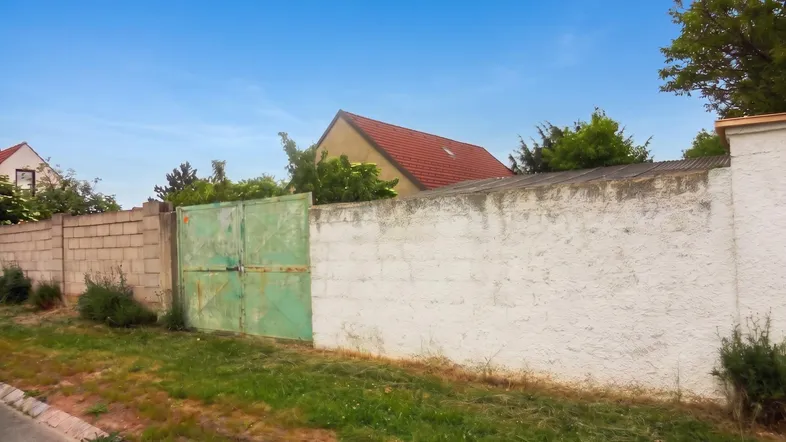 Alte Grundstücksmauer mit verwittertem grünen Tor und Blick auf ein Wohnhaus.