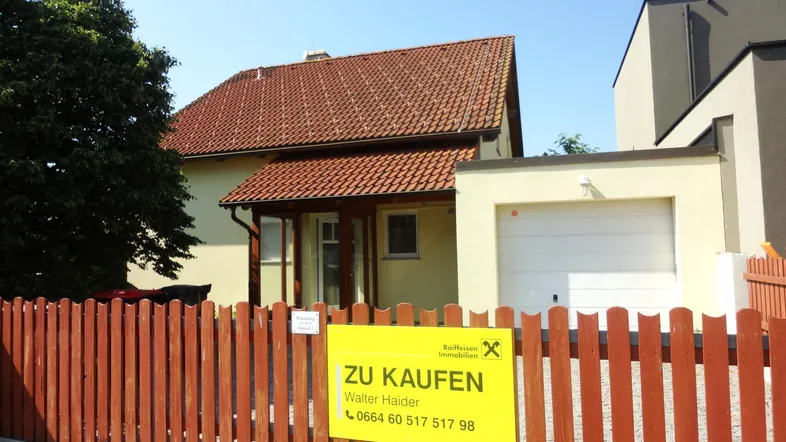 Vorderansicht des Hauses mit Vorgarten, Holzzaun und einem Verkaufsschild.