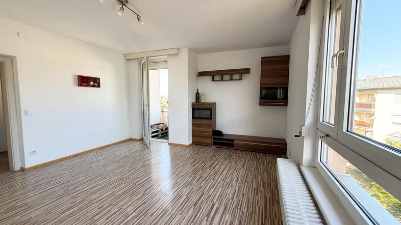 Helles Wohnzimmer mit Laminatboden, großen Fenstern und Zugang zu einem kleinen Balkon.