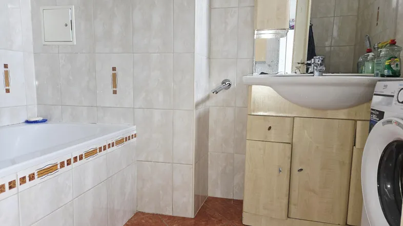 Badezimmer mit Eckbadewanne, Waschbecken, Waschmaschine und hellen Fliesen.