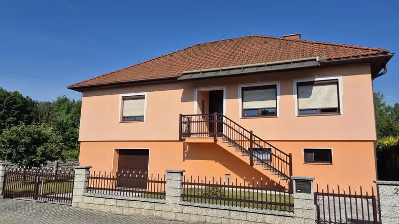 Vorderansicht des Hauses mit Außentreppe, umzäuntem Vorgarten und Satteldach.