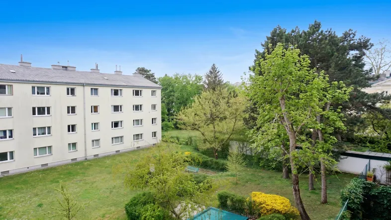 Mehrfamilienhaus mit großer Grünfläche und altem Baumbestand im Außenbereich.