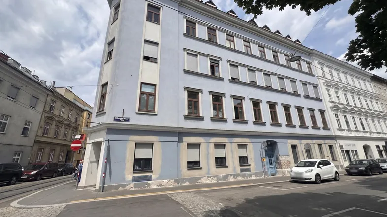 Eckgebäude mit hellblauer Fassade und vielen Fenstern an einer städtischen Straße.