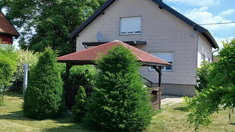 Gepflegter Gartenbereich mit Rasenfläche, Nadelbäumen und einem Holzpavillon neben dem Haus.