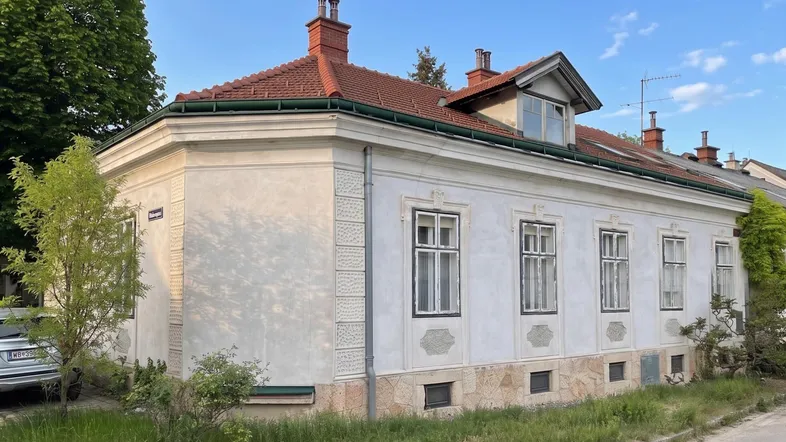 Historisches Gebäude mit heller Fassade, roten Dachziegeln und traditionellen Fenstern.