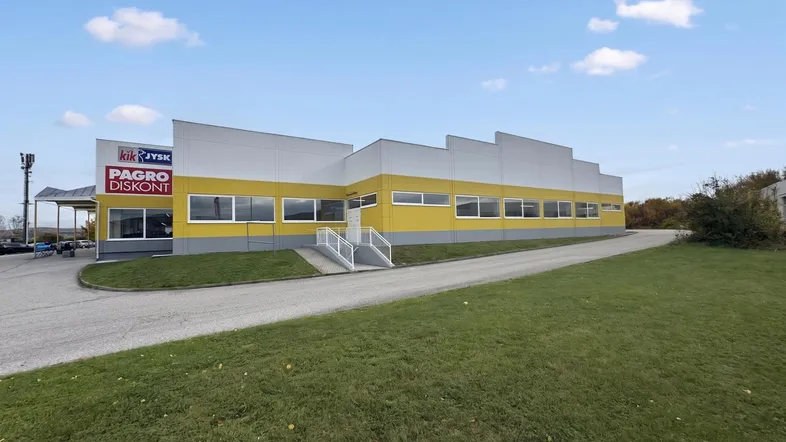Modernes Geschäftsgebäude mit gelb-grauer Fassade, großen Fenstern und weitläufiger Grünfläche davor.