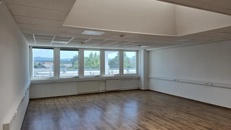 Geräumiger Büroraum mit großen Fenstern, die viel Tageslicht hereinlassen und einen weiten Blick bieten.