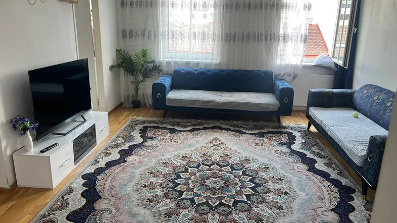 Gemütliches Wohnzimmer mit zwei blauen Sofas, großem Teppich und Holzboden.