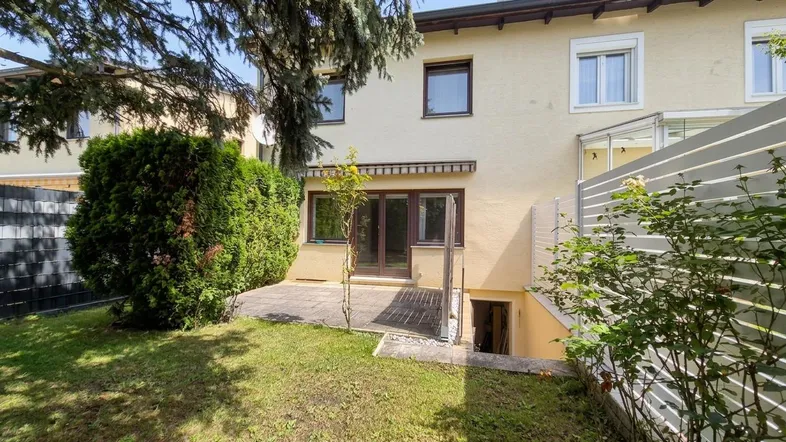 Hinteransicht des Hauses mit kleiner Terrasse, Rasenfläche und Zugang zum Keller.