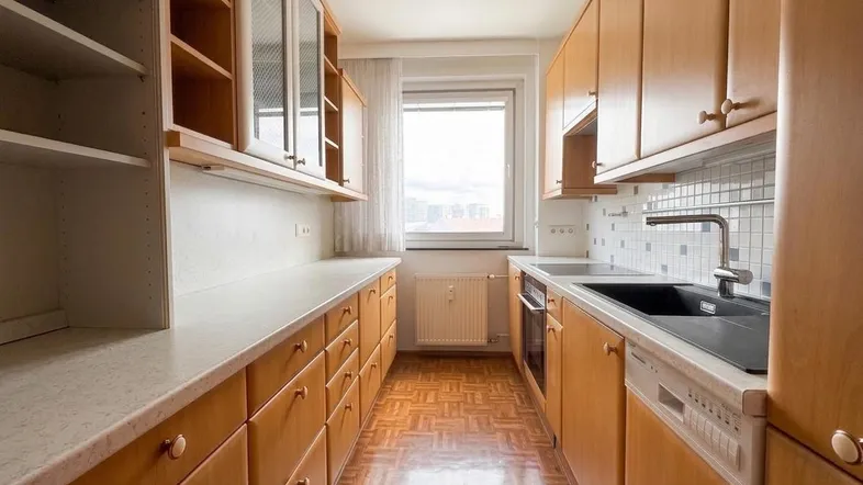 Helle Küche mit Holzschränken, Parkettboden und Fenster mit Blick nach draußen.