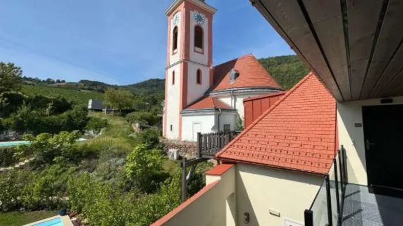 Blick von einer Terrasse mit Pool auf eine historische Kirche und die umliegende Landschaft.