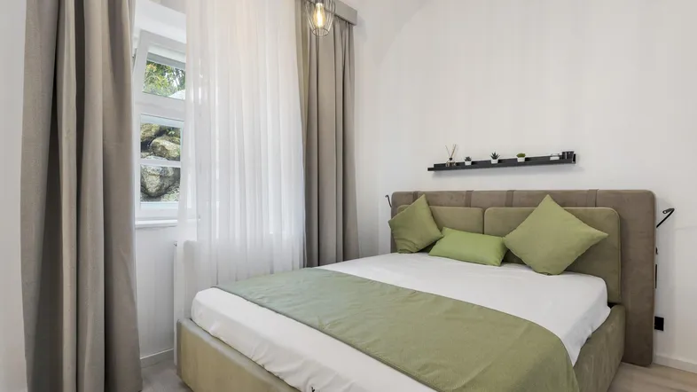 Helles Schlafzimmer mit bequemen Bett, modernen Leuchten und Blick ins Grüne.