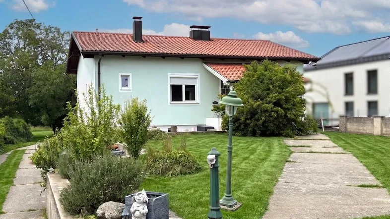 Einfamilienhaus mit hellgrüner Fassade, rotem Ziegeldach und gepflegtem Vorgarten.