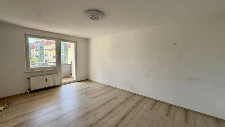 Helles Zimmer mit Laminatboden, weißen Wänden und Zugang zu einem Balkon.