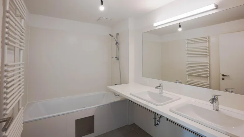 Modernes Badezimmer mit Doppelwaschbecken, Badewanne und beheiztem Handtuchhalter in hellen Farbtönen.