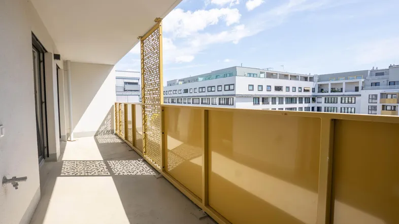 Heller Balkon mit gelbem Geländer und Blick auf moderne Wohngebäude in der Umgebung.