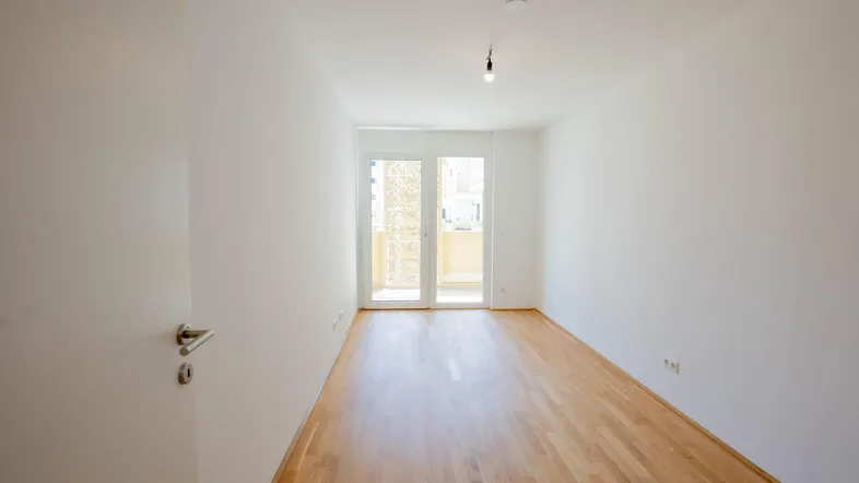 Heller Raum mit Parkettboden und Zugang zu einem Balkon, ideal als Wohn- oder Schlafzimmer.