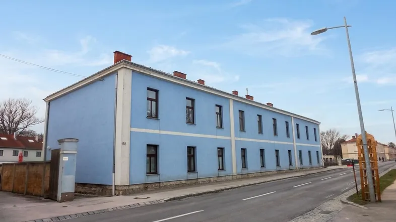 Blau gestrichenes Mehrfamilienhaus an einer Straße unter einem klaren Himmel.