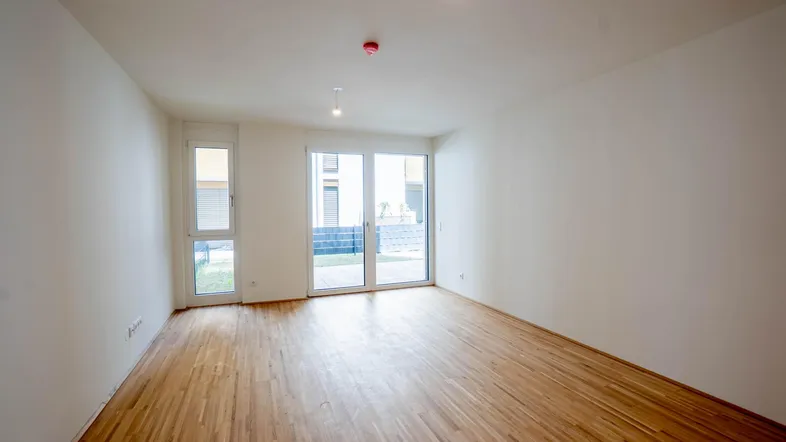 Heller Wohnraum mit Parkettboden und Zugang zu einer Terrasse oder Loggia.