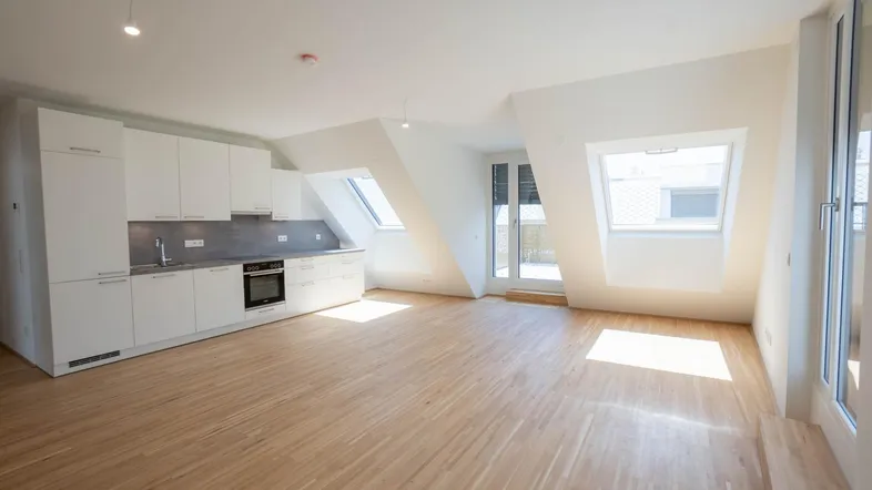 Heller Wohnbereich mit integrierter Küche, Holzboden und großen Dachfenstern unter schrägen Decken.