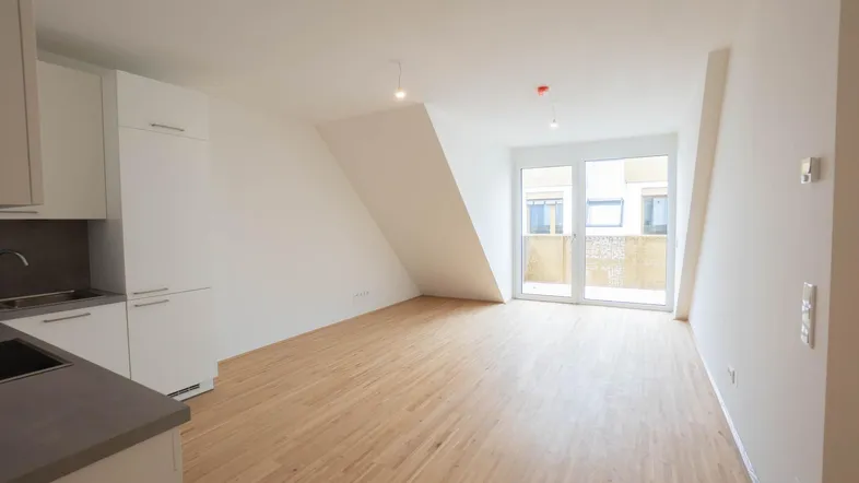 Helles, offenes Zimmer mit Holzboden, Dachschräge und Zugang zu einem Balkon.