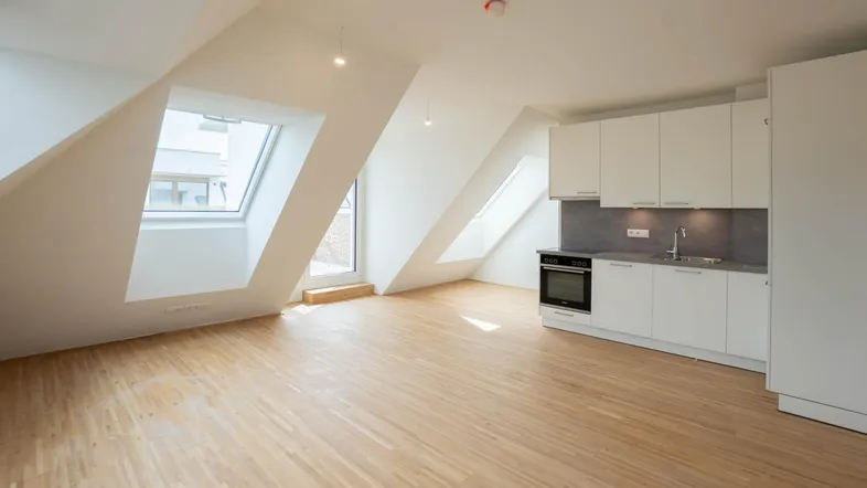 Heller Dachgeschossraum mit kleiner Einbauküche, Holzparkettboden und schrägen Dachfenstern.