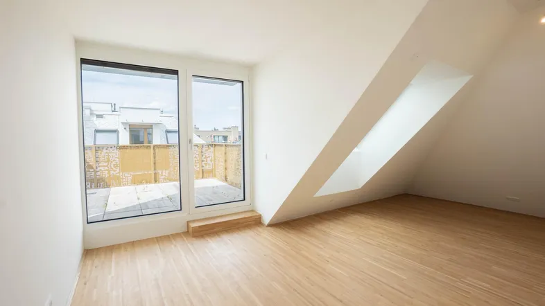 Heller Raum im Dachgeschoss mit Holzboden, schrägen Wänden und Zugang zu einer Terrasse.