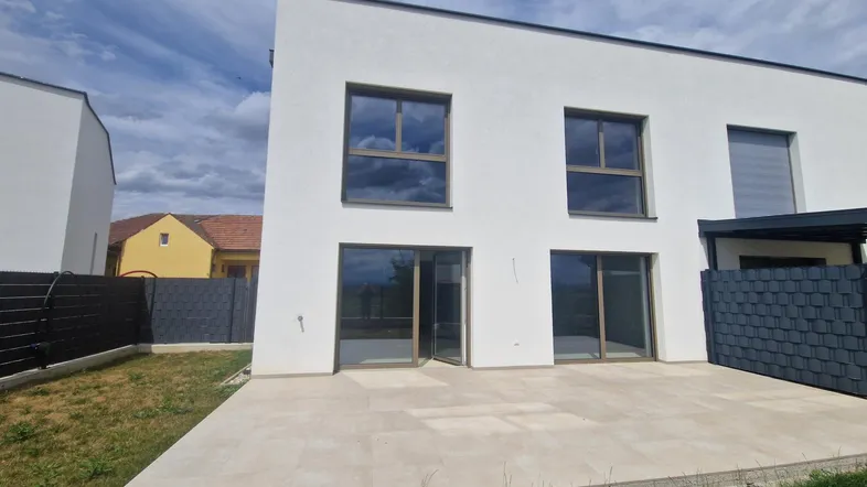 Moderne Hausrückseite mit großer gepflasterter Terrasse und Blick auf die umliegende Landschaft.