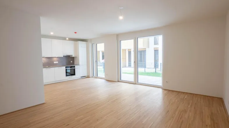 Helles, offenes Wohnzimmer mit integrierter Küche, Parkettboden und Zugang zu einer Terrasse.