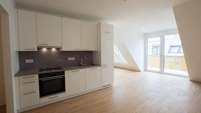 Helle, moderne Einbauküche mit weißen Schränken und Induktionskochfeld in einem offenen Wohnbereich mit Holzboden und Dachschrägen.