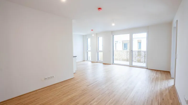 Helles Wohnzimmer mit Parkettboden und Zugang zu einem Balkon oder einer Terrasse.