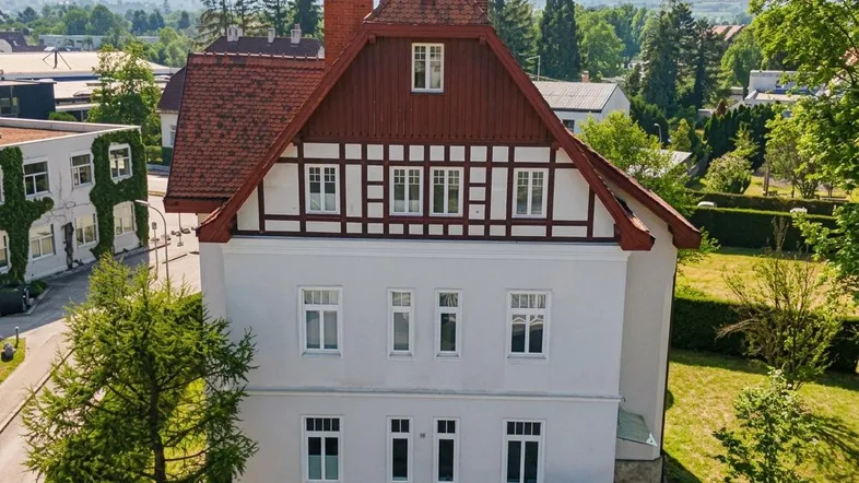 Ansicht der Hausfassade mit traditionellen Elementen, roten Ziegeln und Fachwerkgiebel, umgeben von grüner Landschaft.