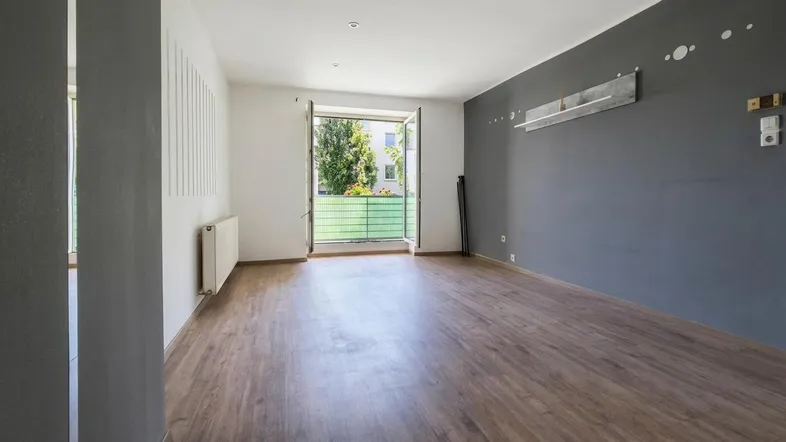 Helles Wohnzimmer mit Holzboden und Zugang zu einem Balkon, teilweise dunkelgrau gestrichen.