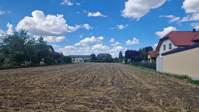 Weitläufiges Grundstück mit Ackerland unter blauem Himmel, umgeben von ländlicher Bebauung.