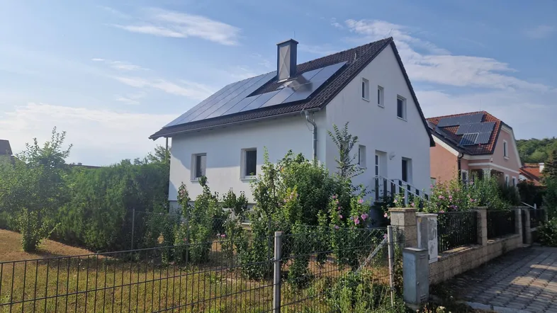 Weißes Einfamilienhaus mit Satteldach und Photovoltaikanlage auf dem Dach.