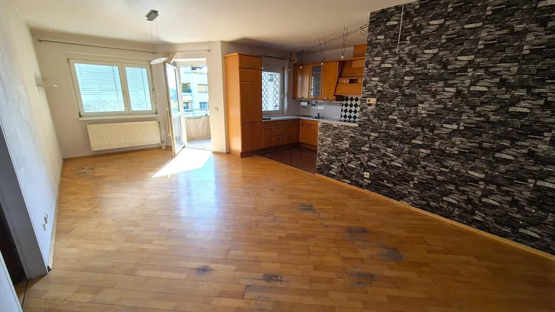 Helles Wohnzimmer mit integrierter Küche, Parkettboden und Zugang zum Balkon.