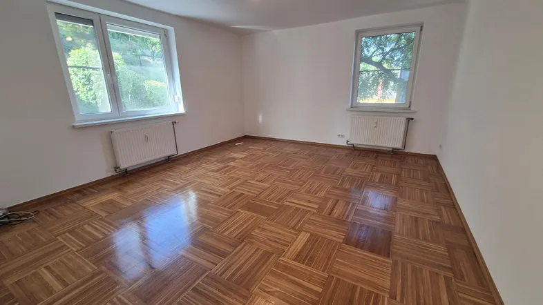 Helles, leeres Zimmer mit Parkettboden und zwei Fenstern, ideal als Wohn- oder Schlafzimmer.