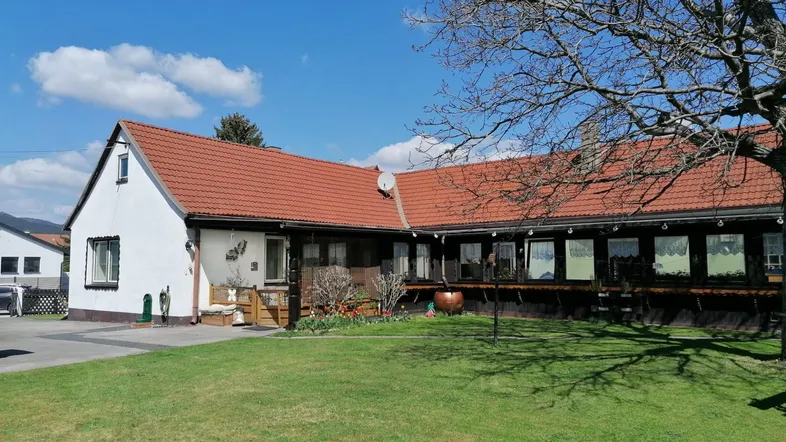 Weißes Haus mit rotem Ziegeldach, grünem Rasen und einem großen Baum im Vorgarten.