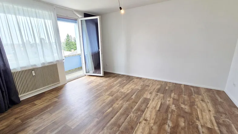 Geräumiges Wohnzimmer mit Laminatboden und Zugang zu einem Balkon, hell und einladend.