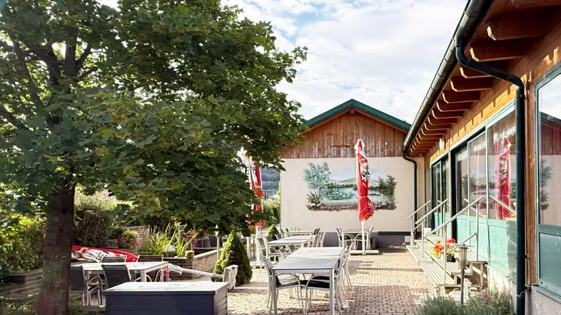 Geräumige Außenterrasse mit Tischen und Stühlen unter Bäumen, ideal für Mahlzeiten im Freien.