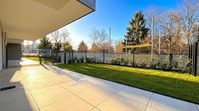 Sonnige Terrasse mit großformatigen Fliesen und angrenzendem Rasenbereich.
