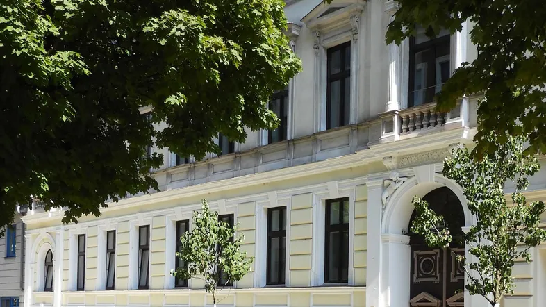 Klassisches Mehrfamilienhaus mit eleganter Fassade und hohen Fenstern, umgeben von Bäumen.