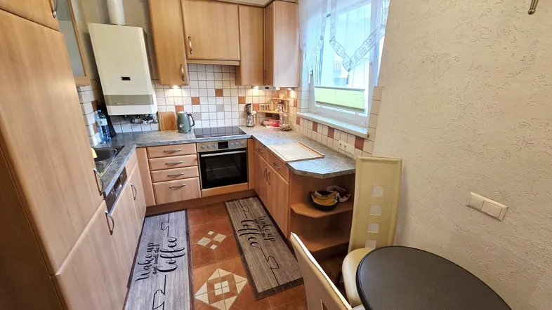 Funktionale Küche mit hellen Holzschränken, Fliesenboden und Fenster für Tageslicht.