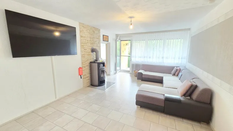 Geräumiges Wohnzimmer mit modernem Kaminofen, Fliesenboden und Zugang zum Balkon.